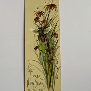 May include: A rectangular bookmark featuring a vintage-style illustration of a green and orange insect perched on tall grasses and dried flowers. The text "FAIR NEW YEAR BE THINE" is printed in decorative script at the bottom left corner.