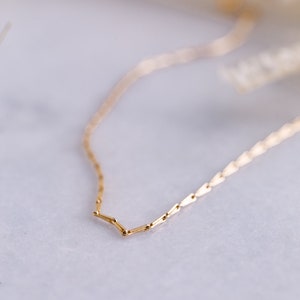May include: A delicate gold chain necklace with a simple, minimalist design. The chain is made of small, linked pieces that create a subtle shimmer.