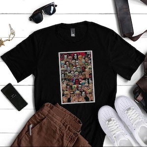Op de afbeelding: Zwart T-shirt met een grafische print van een collage van gezichten van worstelaars. De print is in een rechthoekig frame en toont een verscheidenheid aan worstelaars met verschillende kapsels en gezichtsuitdrukkingen.