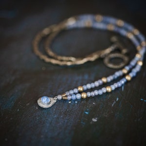 Può includere: Una collana di perline blu e dorate con un ciondolo con una pietra preziosa blu.