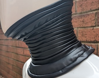 May include: A black faux leather choker with a pleated design. The choker is made of a soft, pliable material and has a smooth finish.