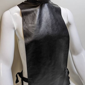 May include: A black leather collar with a high neck and a long, flowing piece of fabric that hangs down the front of the body. The collar has a ribbed texture and is secured with a tie at the back.