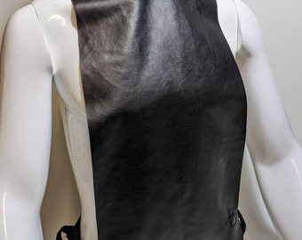 May include: A black leather collar with a high neck and a long, flowing piece of fabric that hangs down the front of the body. The collar has a ribbed texture and is secured with a tie at the back.