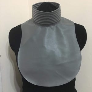 May include: A gray faux leather collar with a ribbed neckline. The collar is displayed on a black mannequin.