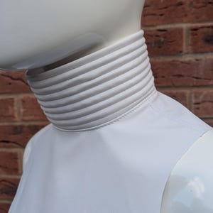 May include: White turtleneck top with a ribbed collar. The collar has a stitched seam around the edge.