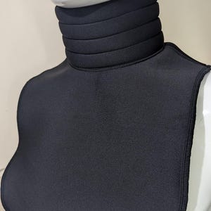 May include: Black neck warmer with a thick, folded collar. The warmer is made of a soft, stretchy fabric.