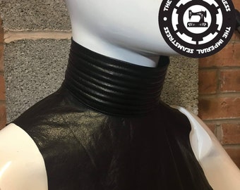 May include: Black leather mock neck collar with a ribbed design. The collar is on a white mannequin.