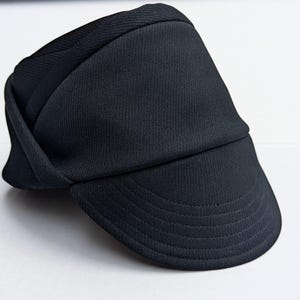 May include: A black, folded, fabric cap with a brim. The cap has a textured, ribbed surface.