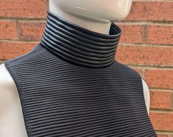 May include: Black mock neck shirt with a black leather collar. The collar has a ribbed texture.