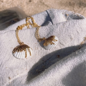 May include: Two gold necklaces with white seashell pendants. The seashells have a gold accent on the top.