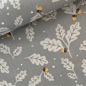 May include: Gray fabric with a repeating pattern of white oak leaves, acorns, and small white stars. The acorns have yellow caps and brown details. The leaves have black veins. The fabric is folded over, showing the pattern in a layered effect.
