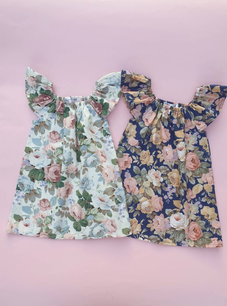 K&ouml;nnte beinhalten: Zwei Kleider mit Blumenmuster, off-shoulder-Ausschnitt und R&uuml;schen&auml;rmeln. Das Kleid links ist hellgr&uuml;n mit einem rosa-wei&szlig;en Blumenmuster. Das Kleid rechts ist dunkelblau mit einem rosa-wei&szlig;en Blumenmuster.
