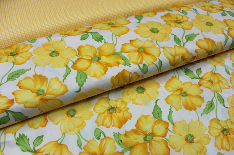 May include: Fabric with a floral pattern of yellow flowers and green leaves on a white background. A second fabric with a yellow gingham pattern is visible in the background.