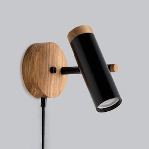 May include: A black and wood wall-mounted light fixture with a cylindrical shade and a cord.