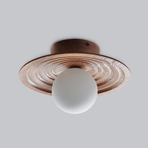May include: A wooden ceiling light fixture with a circular, textured, brown wood shade and a white frosted glass globe.