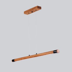 May include: A wooden pendant light fitting with a long, rectangular, brown wood bar and black end caps. The light fitting is suspended from the ceiling by two cords.