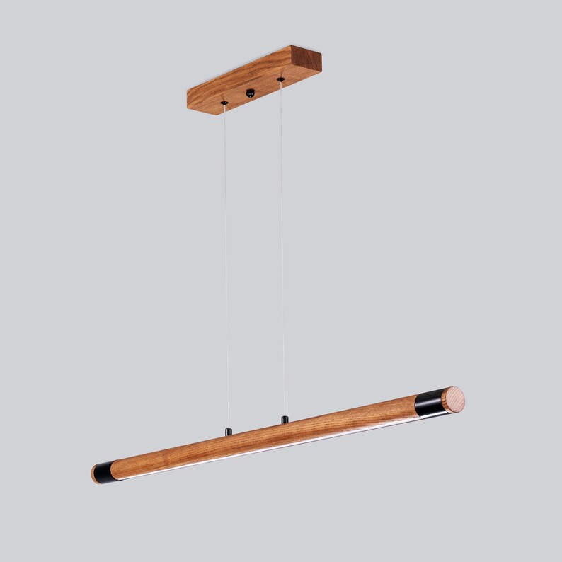 May include: A wooden pendant light fitting with a long, rectangular, brown wood bar and black end caps. The light fitting is suspended from the ceiling by two cords.