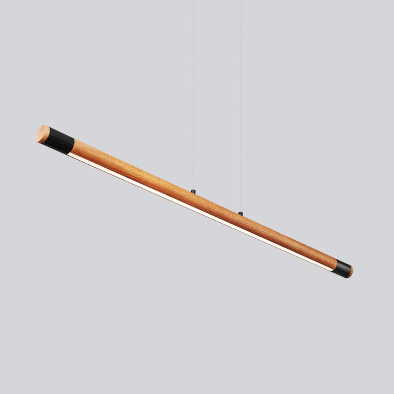May include: A long, wooden pendant light fitting with black end caps. The light is suspended from the ceiling by two thin wires.