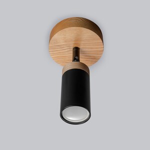 May include: A black and wood ceiling light fixture with a round wooden canopy and a cylindrical black shade. The light has a white diffuser.
