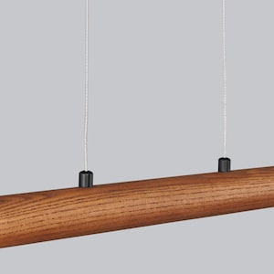 May include: A wooden pendant light fitting with two black cords hanging from the ceiling. The fitting is made of a long, cylindrical piece of wood with a natural brown finish.