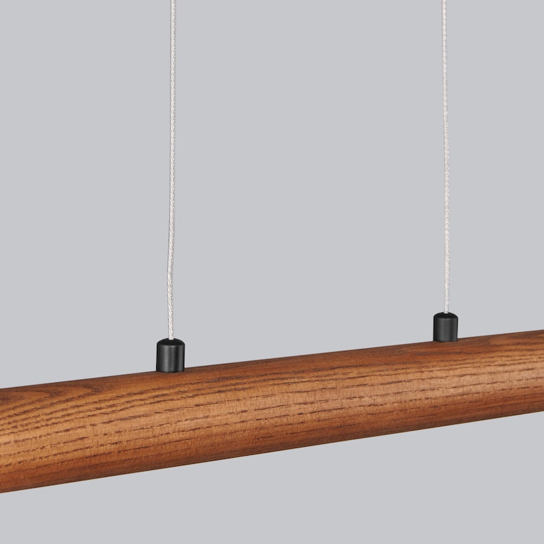 May include: A wooden pendant light fitting with two black cords hanging from the ceiling. The fitting is made of a long, cylindrical piece of wood with a natural brown finish.