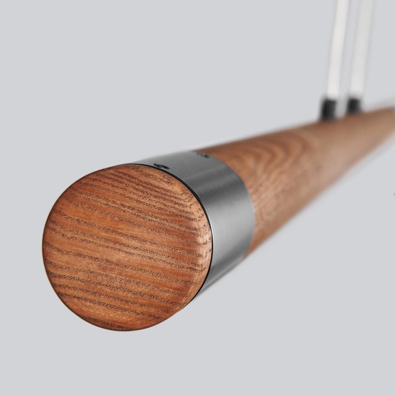 May include: Close-up of a wooden pendant light fitting with a metal cap. The wood has a natural grain pattern and the metal cap is a dark grey colour.