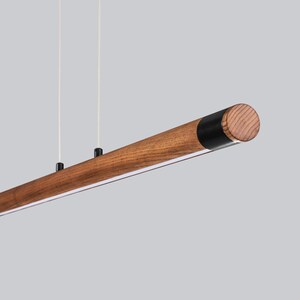 May include: A wooden pendant light fitting with a black accent at the end. The light is suspended from the ceiling by two cords.