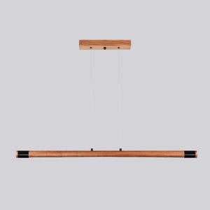 May include: A wooden pendant light fixture with a long, rectangular, brown wood shade and black end caps. The light fixture is suspended from the ceiling by two cords.