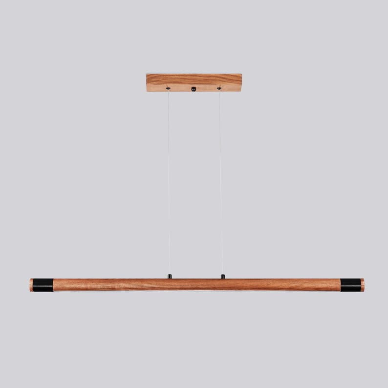 May include: A wooden pendant light fitting with a long, rectangular, brown wood shade and black end caps. The light fitting is suspended from the ceiling by two cords.