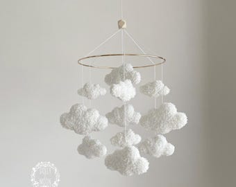 May include: A white cloud mobile with a gold metal ring and a wooden top. The mobile is hanging from the ceiling and has nine fluffy white clouds.