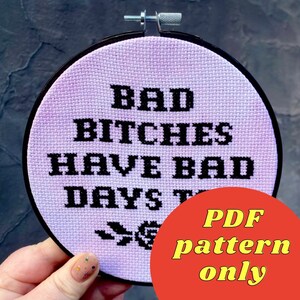 Può includere: Un cerchio da ricamo a punto croce viola e bianco con il testo "Bad Bitches Have Bad Days Too" in filo nero. Il cerchio è tenuto in una mano. Il testo "PDF pattern only" è in giallo su un cerchio rosso.