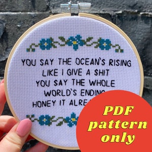 May include: A white embroidery hoop with a cross-stitch design that reads "You say the ocean's rising like I give a shit. You say the whole world's ending honey it alre..."  The hoop is surrounded by a red circle with the text "PDF pattern only" in yellow.