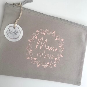 May include: Gray zippered pouch with a pink floral wreath design and the text "Mama Est 2020".