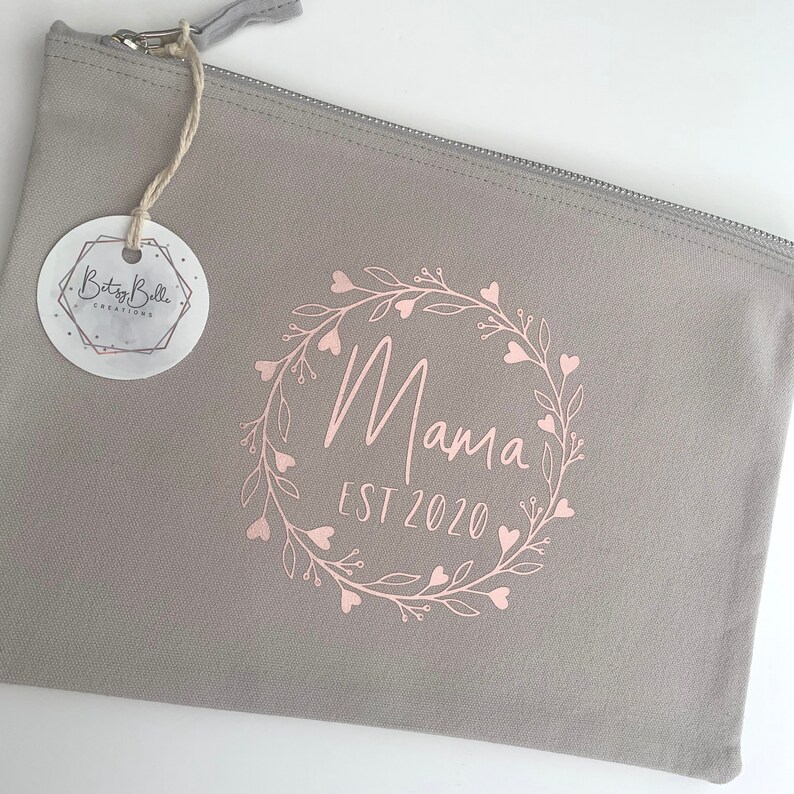 May include: Gray zippered pouch with a pink floral wreath design and the text "Mama Est 2020".