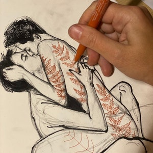 May include: A black ink line drawing on white paper depicting two figures in an embrace. One figure features intricate red fern-like patterns drawn along the back and leg. An orange marker is shown in the process of adding these red details.