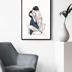 May include: A framed art print featuring a black ink line drawing of two figures embracing. One figure wears a dark blue shirt, while the other has red fern-like patterns on their skin. The artwork is signed by the artist in the bottom right corner.