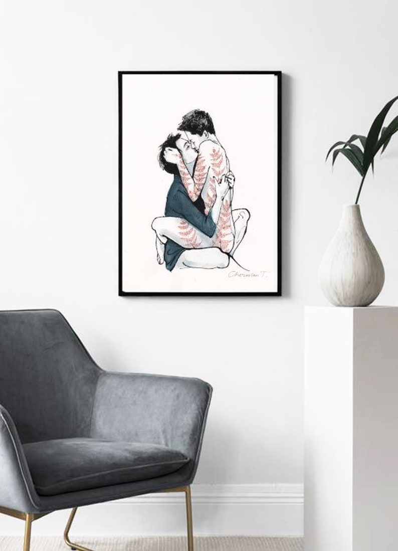 May include: A framed art print featuring a black ink line drawing of two figures embracing. One figure wears a dark blue shirt, while the other has red fern-like patterns on their skin. The artwork is signed by the artist in the bottom right corner.