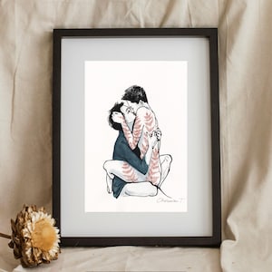 May include: A framed art print featuring a black ink illustration of two figures embracing and kissing. One figure wears a dark blue shirt, while the other has reddish-brown fern-like patterns on their skin. The print is signed Cherwan T.