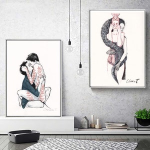 May include: Two framed art prints featuring black and red ink illustrations. The left print shows two figures embracing, one with red fern patterns on their skin. The right print depicts a figure with long dark hair covering their eyes and face.