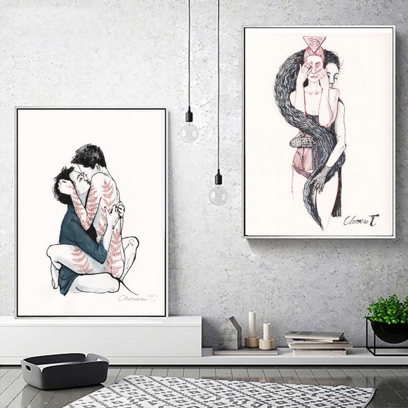 May include: Two framed art prints featuring black and red ink illustrations. The left print shows two figures embracing, one with red fern patterns on their skin. The right print depicts a figure with long dark hair covering their eyes and face.