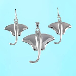 Op de afbeelding: Een set van drie sterling zilveren oorbellen en een hanger met een manta-ray ontwerp. De oorbellen en hanger zijn allemaal in de vorm van een manta-ray, met de vleugels uitgespreid en de staart opgerold.