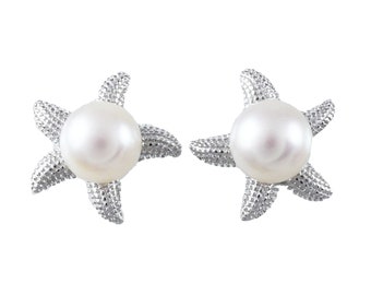 Puede incluir: Un par de pendientes de estrella de mar plateados con una perla blanca en el centro de cada estrella de mar.