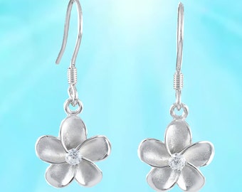 May include: A pair of silver dangle earrings featuring a white flower design with a clear rhinestone in the centre.