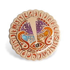 May include: A gold-colored metal pin with a circular design. The center of the pin features a stylized eye with a purple, blue, and orange design. The outer ring of the pin has a repeating pattern of stylized letters.
