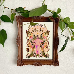 Puede incluir: Una impresión artística enmarcada en un marco ornamental marrón oscuro, que representa una figura desnuda con alas de mariposa y elementos florales. Hojas verdes rodean el marco.