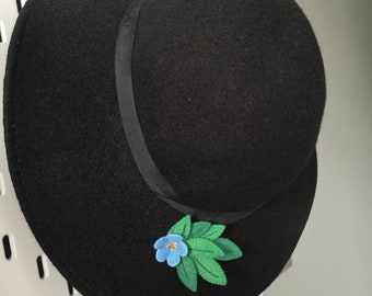 Könnte beinhalten: Ein schwarzer Filzhut mit breiter Krempe und einer blauen und grünen Blumenverzierung.