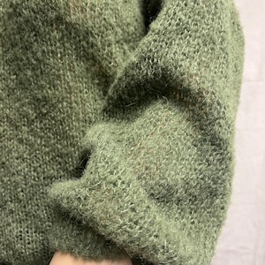 Könnte beinhalten: Ein weicher, grüner Strickpullover mit lockerer, entspannter Passform. Der Pullover hat eine strukturierte, flauschige Optik.