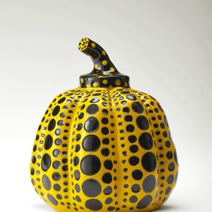 Può includere: Una scultura di zucca in ceramica gialla con pois neri di varie dimensioni. Il gambo è nero con pois gialli. La zucca è un'opera d'arte decorativa, probabilmente per l'arredamento della casa o l'esposizione stagionale.