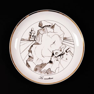 Może przedstawiać: Biały ceramiczny talerz ze złotą obwódką przedstawia czarno-biały rysunek surrealistycznej rzeźby. Talerz jest podpisany "DALI" i zatytułowany "La escultura".