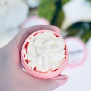 May include: A pink container with a white, creamy substance inside. The container has a textured design.